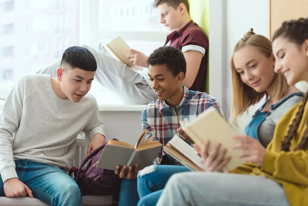 Fünf Jugendliche sitzen über Büchern und lachen